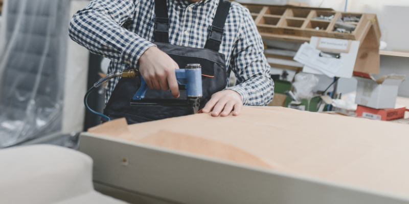 Polsterer befestigt den Spannstoff während einer professionellen Polsterarbeit in der Werkstatt.